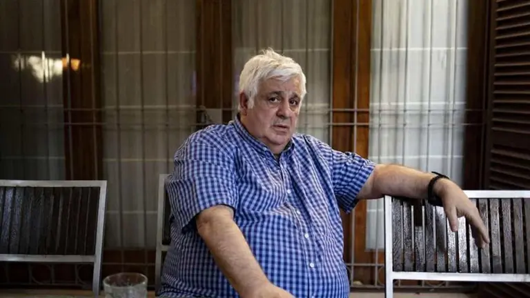 Claudio Samid sentado entre medio de sillas en una habitación